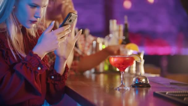 Fiatal nő ül a pultos standnál, és használja a telefonját - fényképez az italról — Stock videók