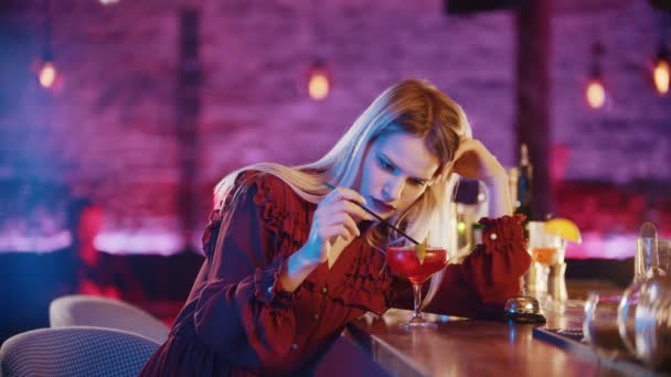 Linda jovem entediada sentada ao lado do barman stand e mexe a bebida com uma palha — Vídeo de Stock