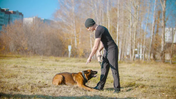 Um homem a treinar o seu cão pastor alemão para se sentar no chão — Fotografia de Stock