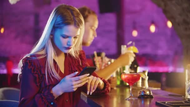 年轻的金发女人坐在酒吧间旁边用她的电话 — 图库视频影像