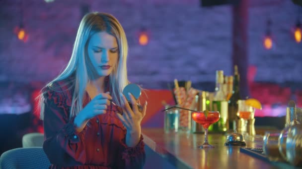 Красивая молодая женщина сидит у барменской стойки и наносит красную помаду на губы — стоковое видео