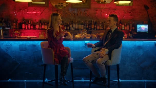 Um casal tendo um encontro no bar - sentado nas cadeiras do bar em direção à câmera - bebendo suas bebidas e conversando — Vídeo de Stock