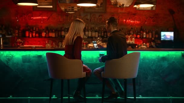 Un couple envoûtant ayant un rendez-vous dans le bar assis près du stand et regardant les photos au téléphone — Video
