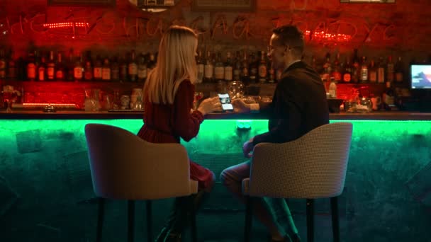 若いカップルがバーでデートをしている-スタンドに座って電話で写真を見て — ストック動画