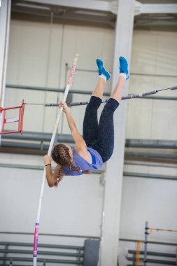 Kapalı alanda sırıkla atlama - örgülü saçları olan genç kadın bölmenin üzerinden atlıyor