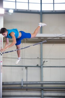 Kapalı alanda sırıkla atlama - genç adam bölmenin üzerinden uçuyor