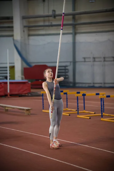 Pole vaulting indoors - young woman is standing with pole in hands — Stock Photo, Image