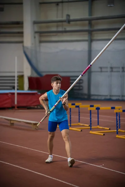 Pole vaulting indoors - young man standing on the runway holding a pole — Stock Photo, Image