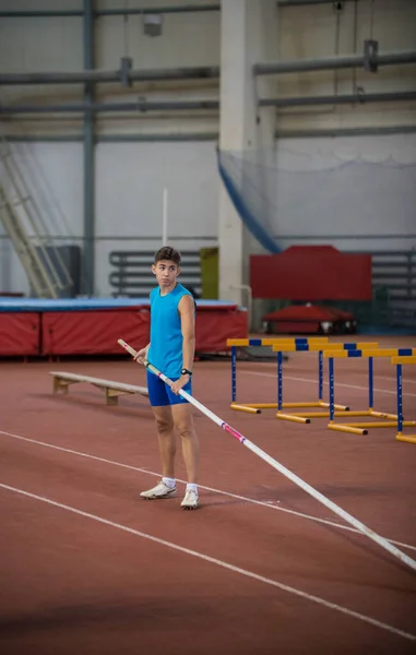 Pole vaulting indoors - young man in blue shirt standing on the runway holding a pole — Stock Photo, Image