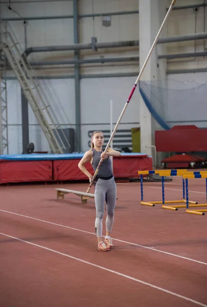 Skok na tyč uvnitř - mladá žena drží tyč a dívá se na ni — Stock fotografie