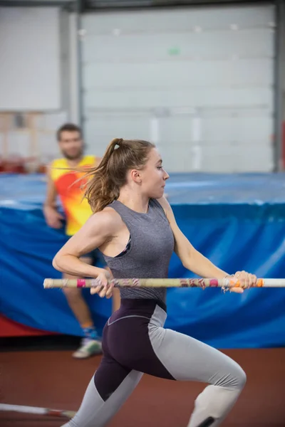 Pole vaulting indoors - young sportive woman with ponytail running with a pole in the hands — 图库照片
