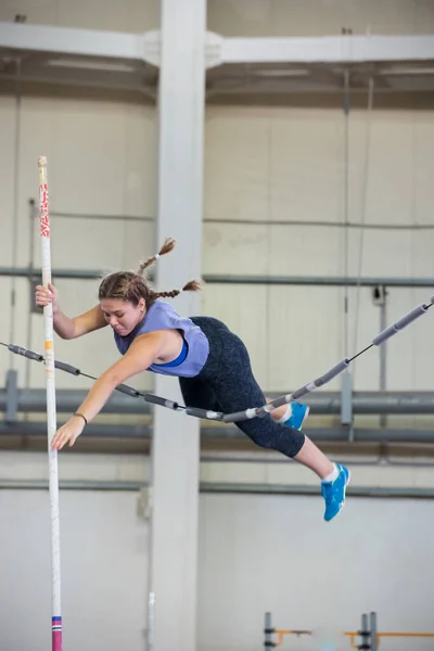 Pole vaulting indoors - young woman with pigtails jumping over the partition trying not to touching it — Stock Photo, Image