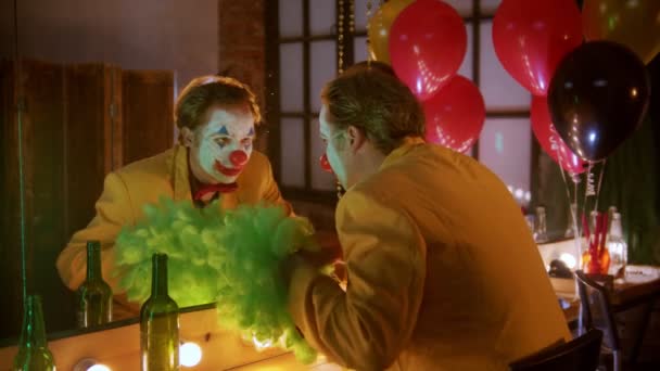 En clown sätter på sig en grön peruk och ler mot spegeln. — Stockvideo