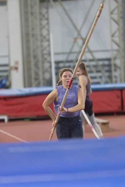 Bóveda de poste en el interior - joven mujer deportiva con coletas corriendo con un poste en las manos —  Fotos de Stock