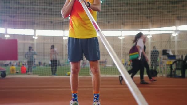 Pole bóveda en el interior - un hombre con camisa amarilla de pie en la pista con un poste - estadio deportivo — Vídeo de stock