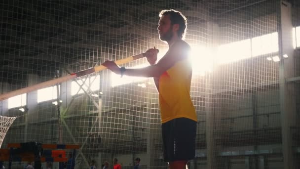 Bóveda de poste en el interior - un hombre con camisa amarilla de pie en la pista con un poste y preparándose para asumir el salto — Vídeos de Stock