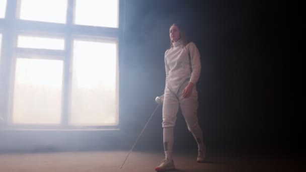 A young woman fencer walking to the fighting area with loose hair in white costume performing basic attack movements — Stock Video