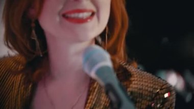 Kapak şarkısı çalan bir müzik grubu. Kırmızı rujlu kızıl bir kadın tutkuyla şarkı söylüyor.