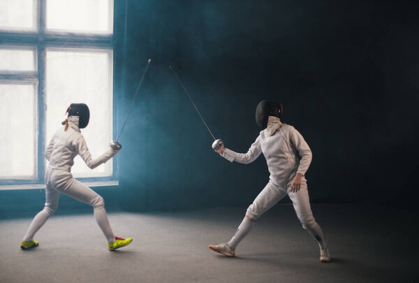 A fencing training in the studio - two women in protective costumes having a duel