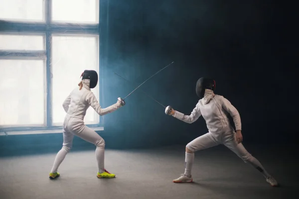 Une formation d'escrime en studio - deux femmes en costumes de protection blancs en duel — Photo