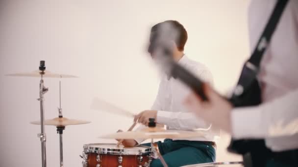 Ένα μουσικό συγκρότημα που παίζει - άνδρες με λευκά πουκάμισα κιθαρίστας και ντράμερ παίζουν τους ρόλους τους — Αρχείο Βίντεο