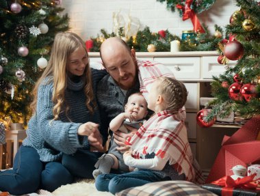Noel konsepti. Mutlu gülümseyen aile ağacın yanında oturuyor.