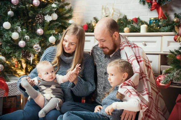 クリスマスのコンセプト-木の近くに座っている小さな子供たちと幸せな家族 — ストック写真