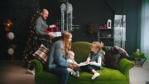 Рождественская концепция - мама с детьми, сидящими на диване - папа приходит к ним и приносит подарки — стоковое видео