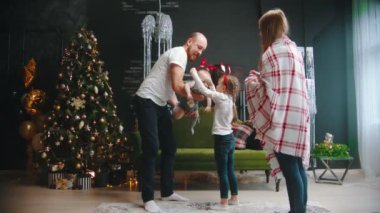 Yeni Yıl - Anne ve baba çocuklarıyla Noel ağacının yanında dans ediyorlar - çocukların kafalarında komik bantlar