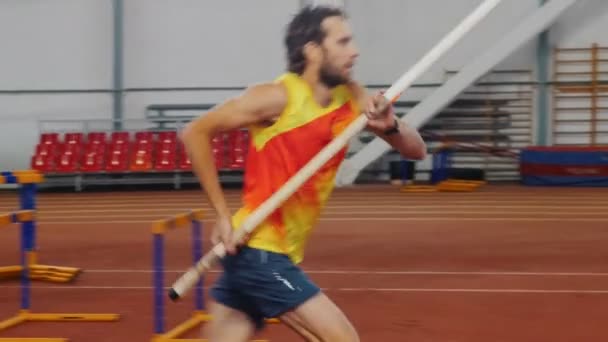 Bóveda de poste en el interior - un hombre con camisa amarilla realizando un salto sobre la barra — Vídeos de Stock