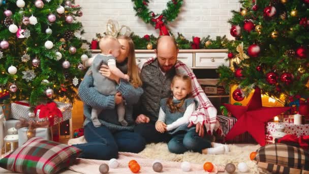 AÑO NUEVO - mamá y papá están sentados con sus hijos bajo una manta riendo y besando — Vídeos de Stock