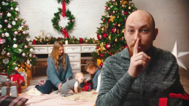 AÑO NUEVO - papá está sacudiendo un regalo poniendo un dedo en sus labios y luego dándoselo a su familia — Vídeo de stock