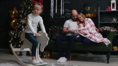 Yeni yıl - aile kanepenin üzerinde battaniyenin altında oturuyor ve kızının yanında oyuncak bir ata biniyor.