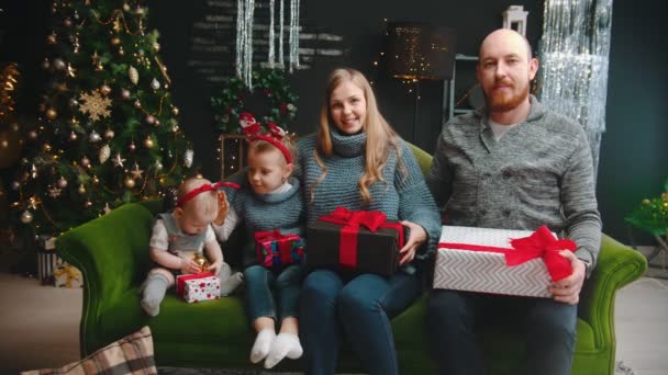 Conceito de Natal - família feliz sentada no sofá segurando presentes - crianças brincando umas com as outras — Vídeo de Stock