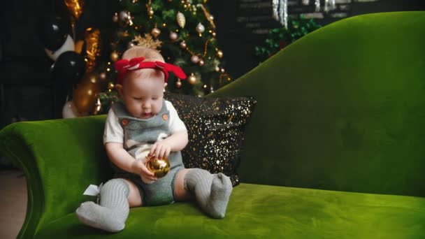 NOVO ANO - bebê e sua mãe está sentada no sofá e brincando com a bola de Natal — Vídeo de Stock