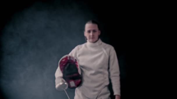 Výcvik šermu - mladá žena šermířka, která vyšla ze tmy a nasadila si ochrannou přilbu - se postaví na pozice a začne bojovat — Stock video