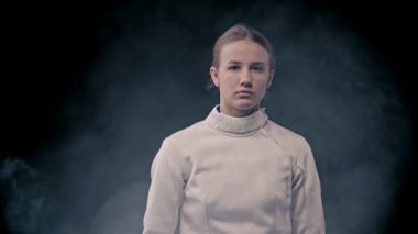 Eskrim antrenmanı. Karanlıktan çıkıp kılıcı omuzlarının arkasına koyan genç bir eskrim ustası.