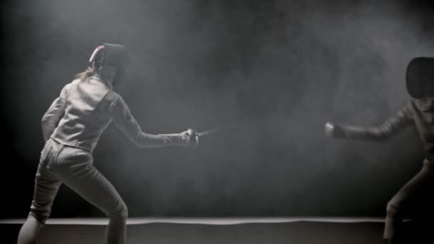 Обучение фехтованию - две молодые женщины, устроившие поединок между собой в дымчатой студии — стоковое видео