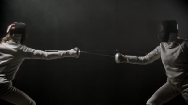 Fencing training - two young women having a duel between each other in the dark smoky studio — Αρχείο Βίντεο