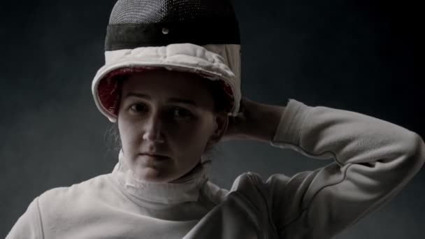 Szkolenie szermierki w ciemnym studio - młoda kobieta zakładająca kask i stojąca w pozycji — Wideo stockowe