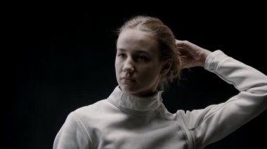 Genç bir eskrimci kadın saçlarını açıyor ve kafasını sallıyor.