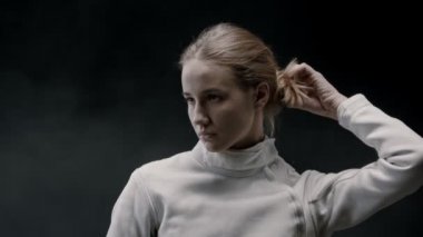 Genç bir eskrimci kadın saçlarını açıyor ve kafasını sallıyor.