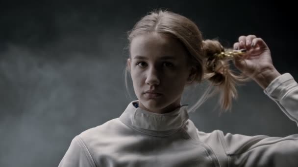 A young pretty woman fencer lets her blonde long hair down and shakes her head — ストック動画