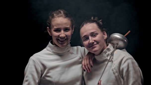 Två unga kvinnor fäktare står i den mörka studion - tittar i kameran — Stockvideo