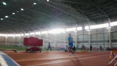 Stadyumda sırıkla atlama eğitimi alan genç bir adam barın üzerinden atlıyor.