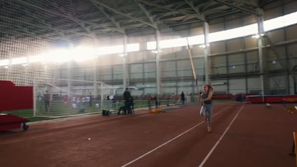 Pole vault training - a young woman with ponytail running up and jumping over the bar - touches the bar — ストック動画