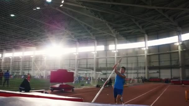 Stabhochsprungtraining im Stadion - ein junger Mann im blauen Hemd springt über die Stange — Stockvideo