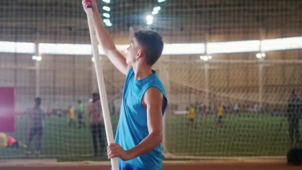 Pole vaulting indoors - a young man in blue shirt raises up the pole up and starts running — Stock Video