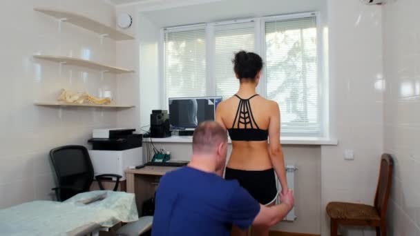 Kiropraktisk behandling - läkaren inspekterar de unga kvinnorna nedre delen av ryggen — Stockvideo