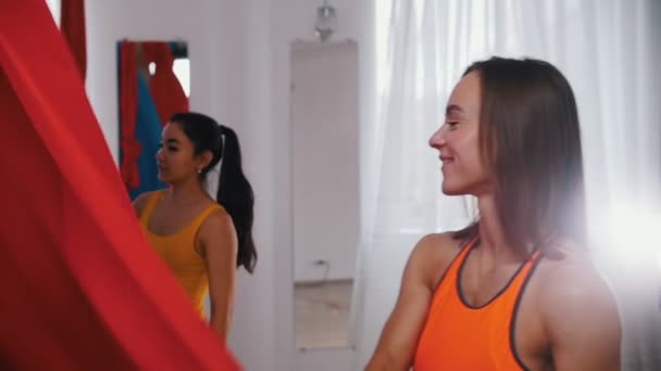 Luchtyoga - Een atletische lachende vrouw die het doek van een rode hangmat voor yoga verspreidt — Stockvideo